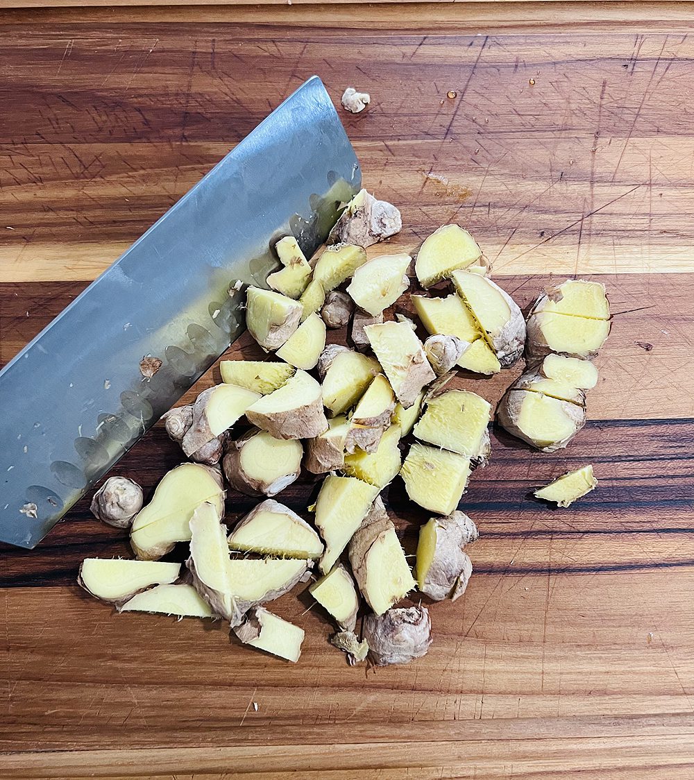 Fresh ginger, chopped on a wooden cutting board with large chef's knife.