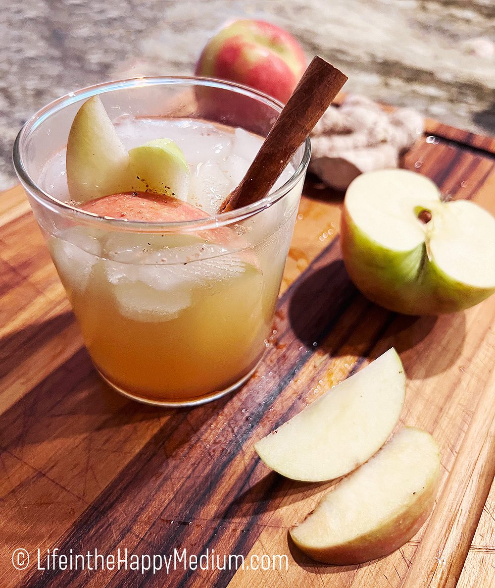 Apple Spice Gin Sour pictured on a wooden cutting board surrounded by cut apples and fresh ginger, with a cinnamon stick.
